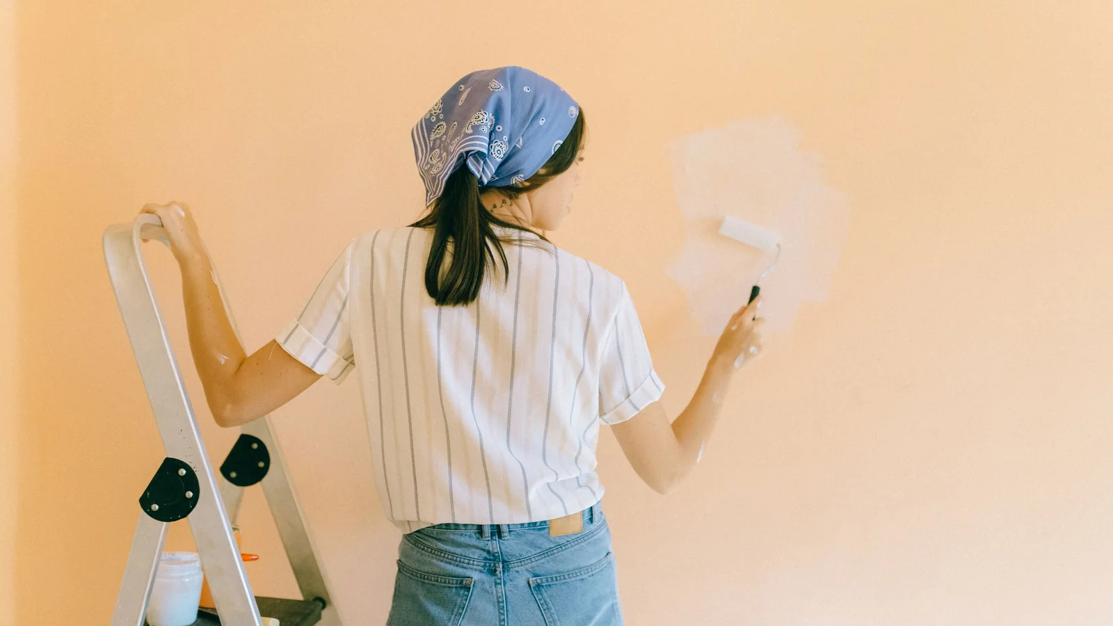 Peinture au rouleau d'un mur couleur pêche, depuis un escabeau