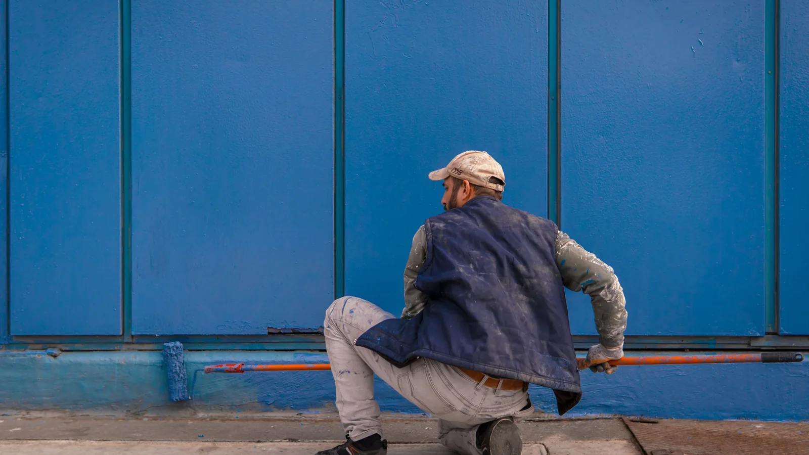 Peintre accroupi appliquant du bleu au rouleau sur un mur extérieur