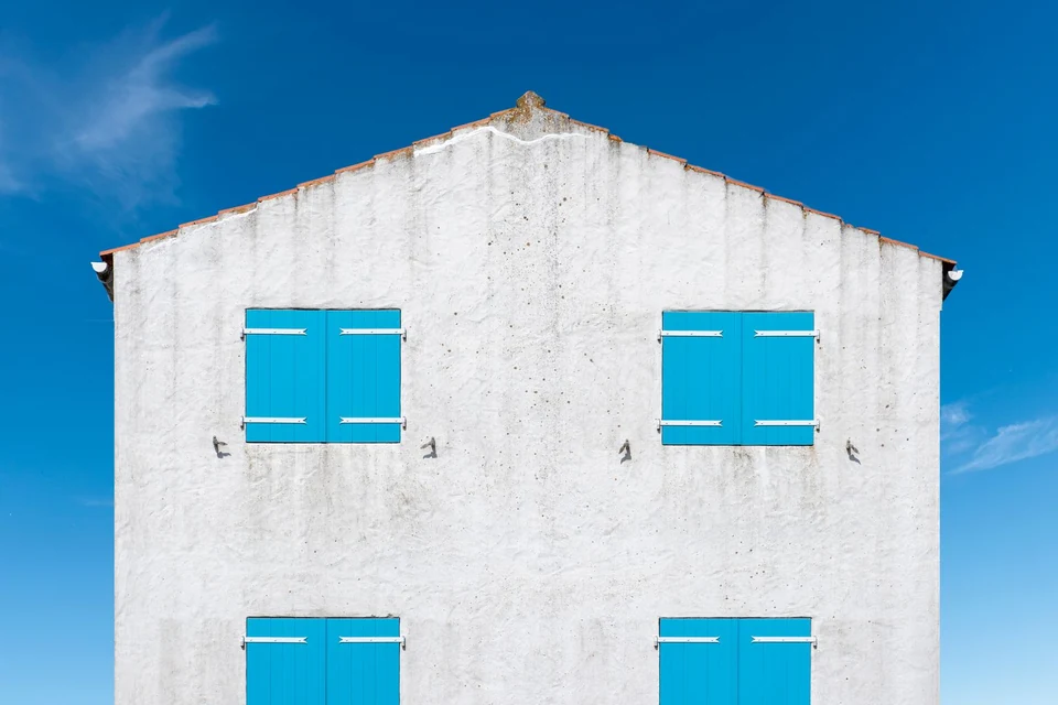 Pignon blanc aux volets turquoise sous un ciel bleu