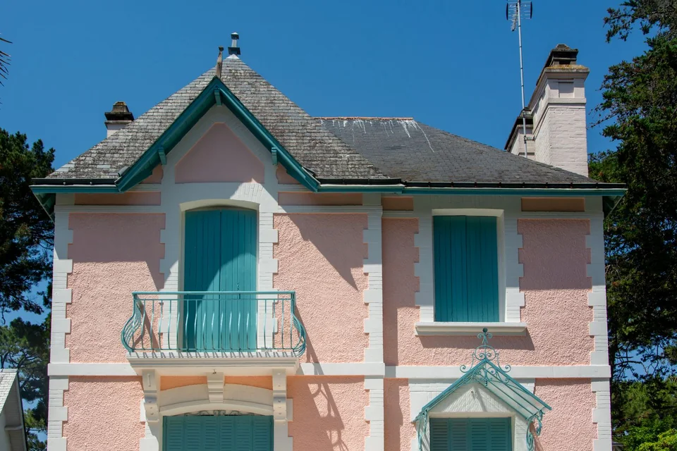 Villa balnéaire rose aux volets verts et balcon en fer forgé